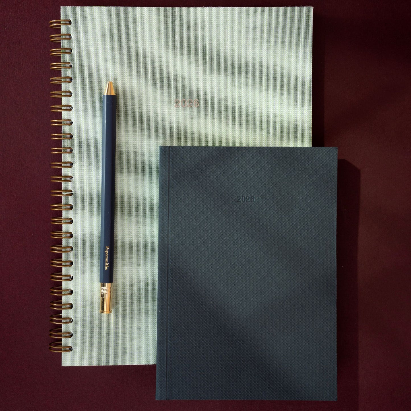 Two 2026 wiro green notebooks and a pen on a dark red background papersmiths