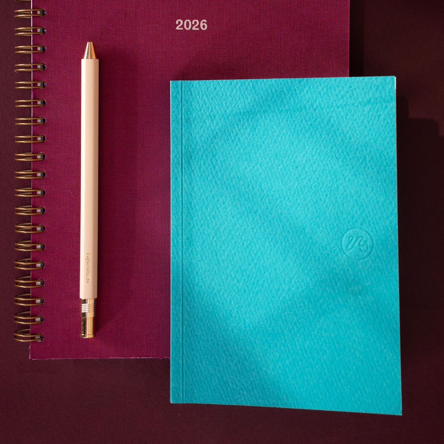 Turquoise notebook with a gold pen on a maroon background