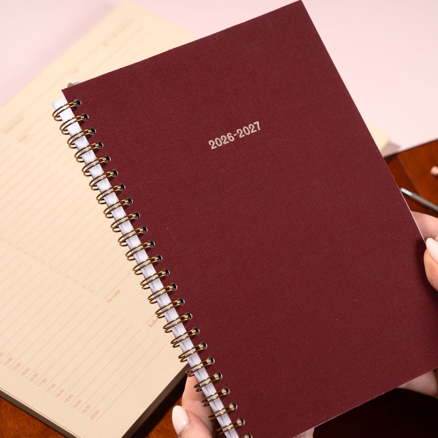 Maroon planner with 2026-2027 text held by a hand on a light background