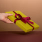 Hand holding a yellow gift box with a red ribbon against a brown background