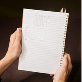 Person holding a spiral-bound planner with a dark background
