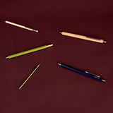 Five retractable mechanical pencils in various colors (beige, light green, navy blue, and silver) arranged on a solid dark red background.