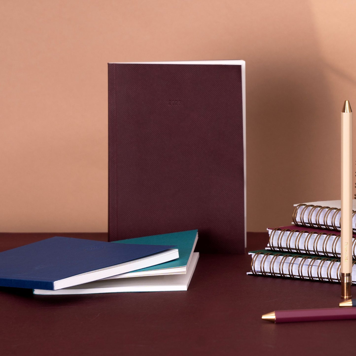 Stack of notebooks and a pen on a brown surface with a beige background