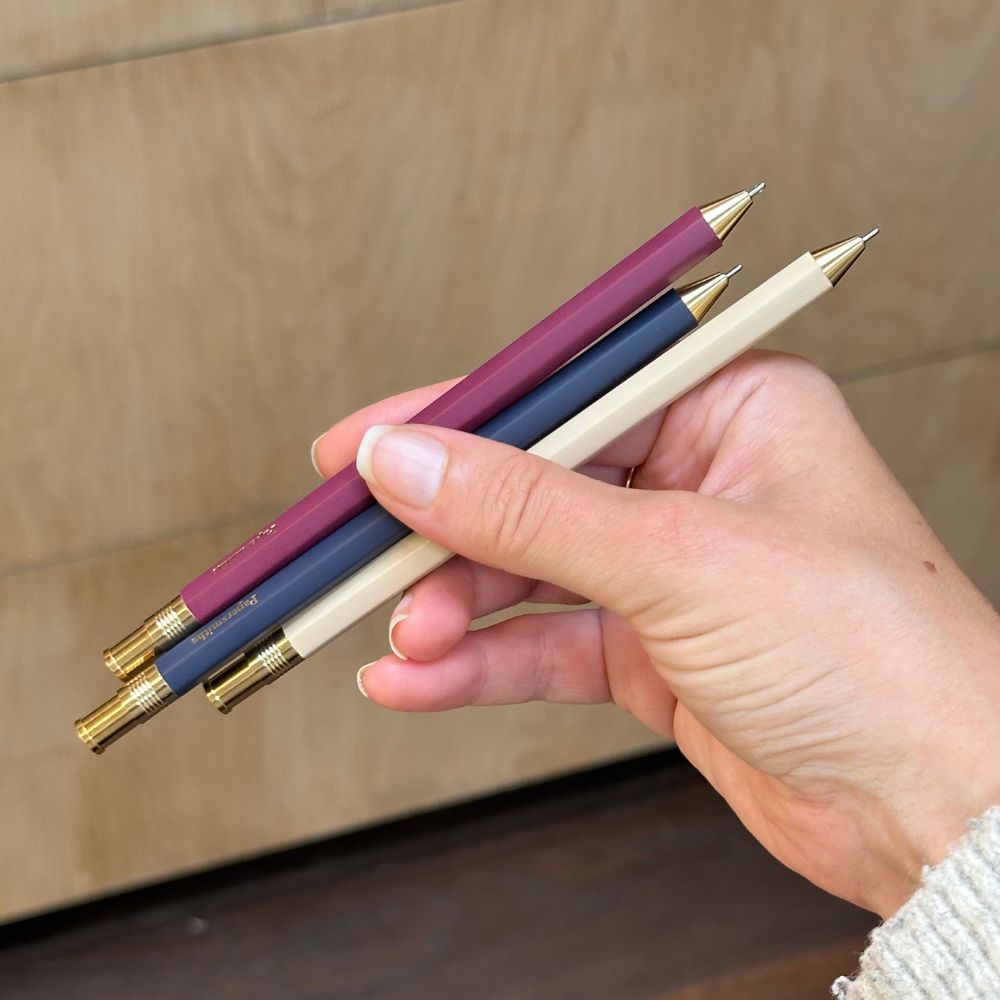 Hand holding three pens with gold caps against a wooden background