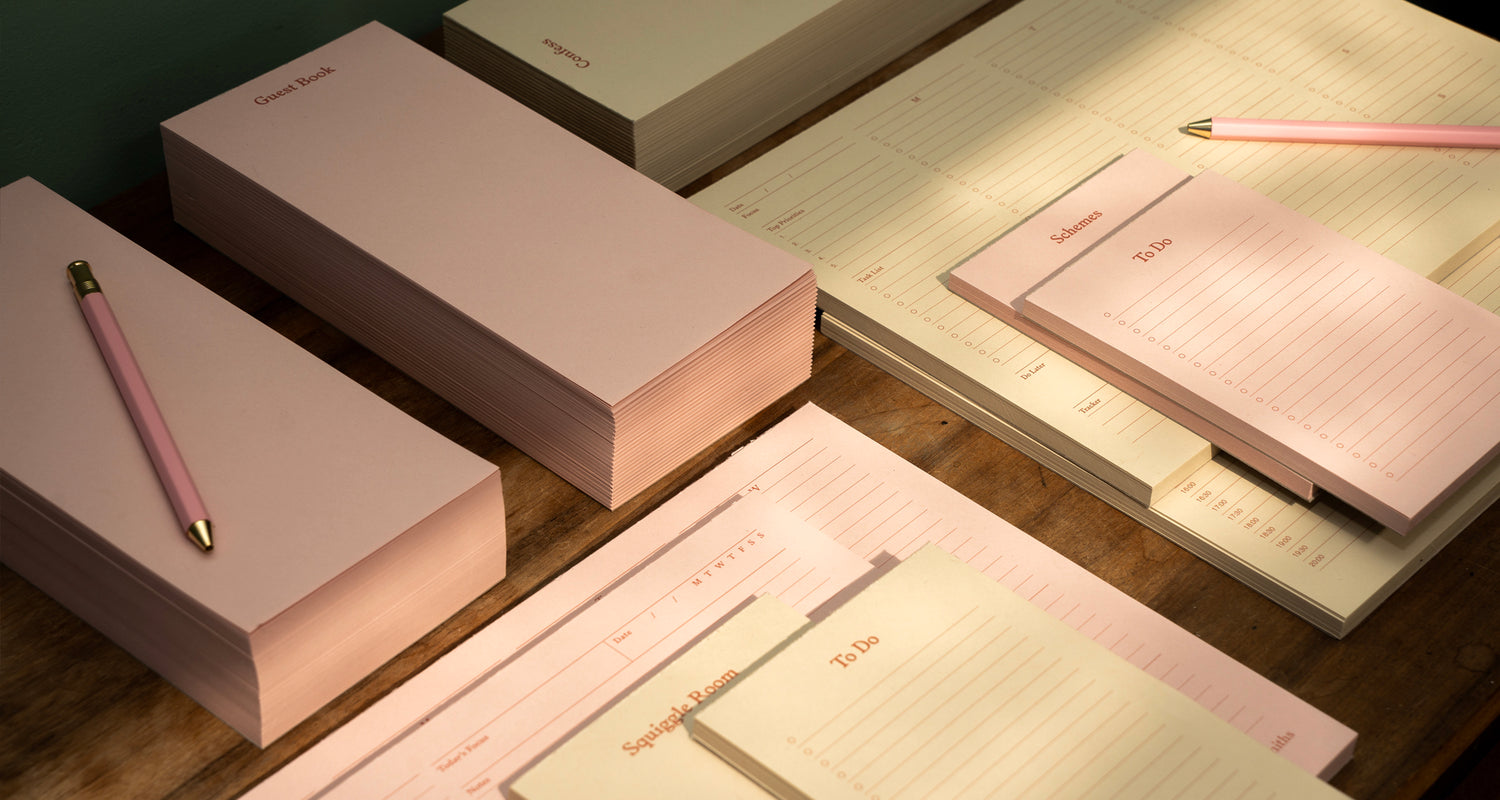 Set of pink notebooks and pens on a wooden surface