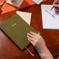 Person holding a green planner on a desk with office supplies.