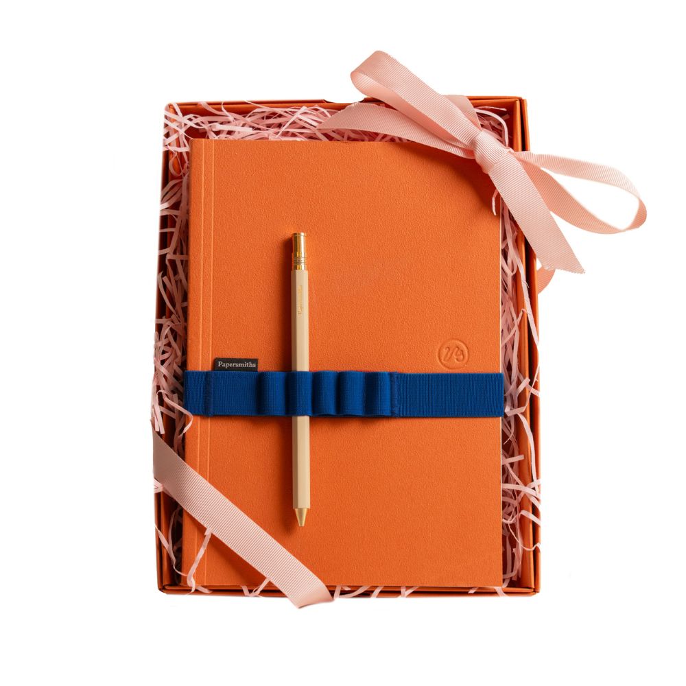 Orange notebook with a pen and ribbon in a decorative box on a white background