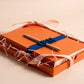 Orange gift box with a gold pen and blue ribbon on a beige background