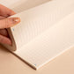 Hand holding an open notebook with lined pages on a beige background