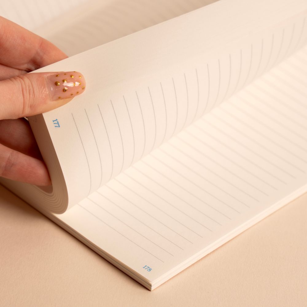 Hand holding an open notebook with lined pages on a beige background