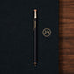 Navy pen with silver and gold accents on a navy surface with a wooden edge