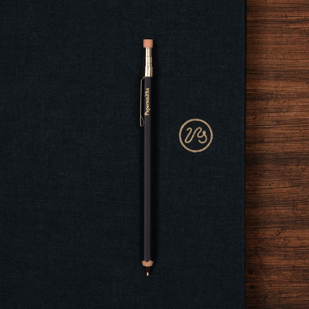 Navy pen with silver and gold accents on a navy surface with a wooden edge
