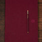 Maroon notebook with a matching pocket pencil on a wooden surface