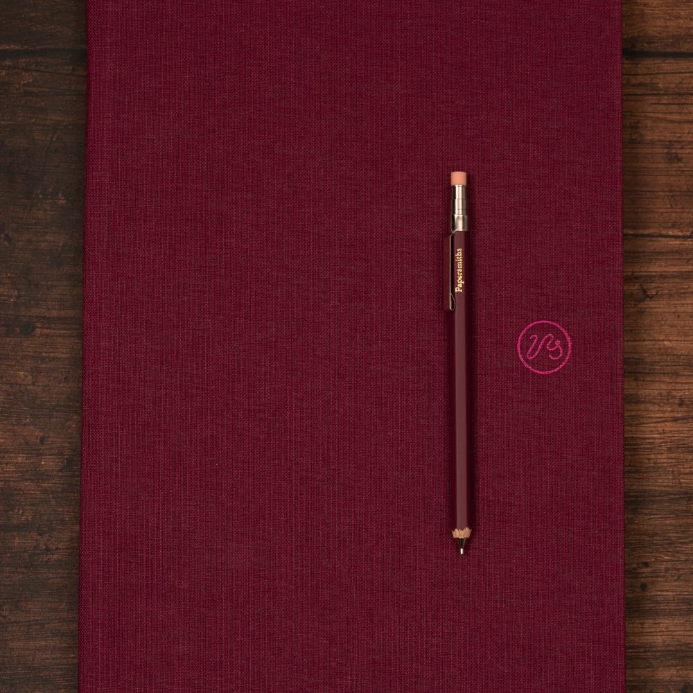 Maroon notebook with a matching pocket pencil on a wooden surface