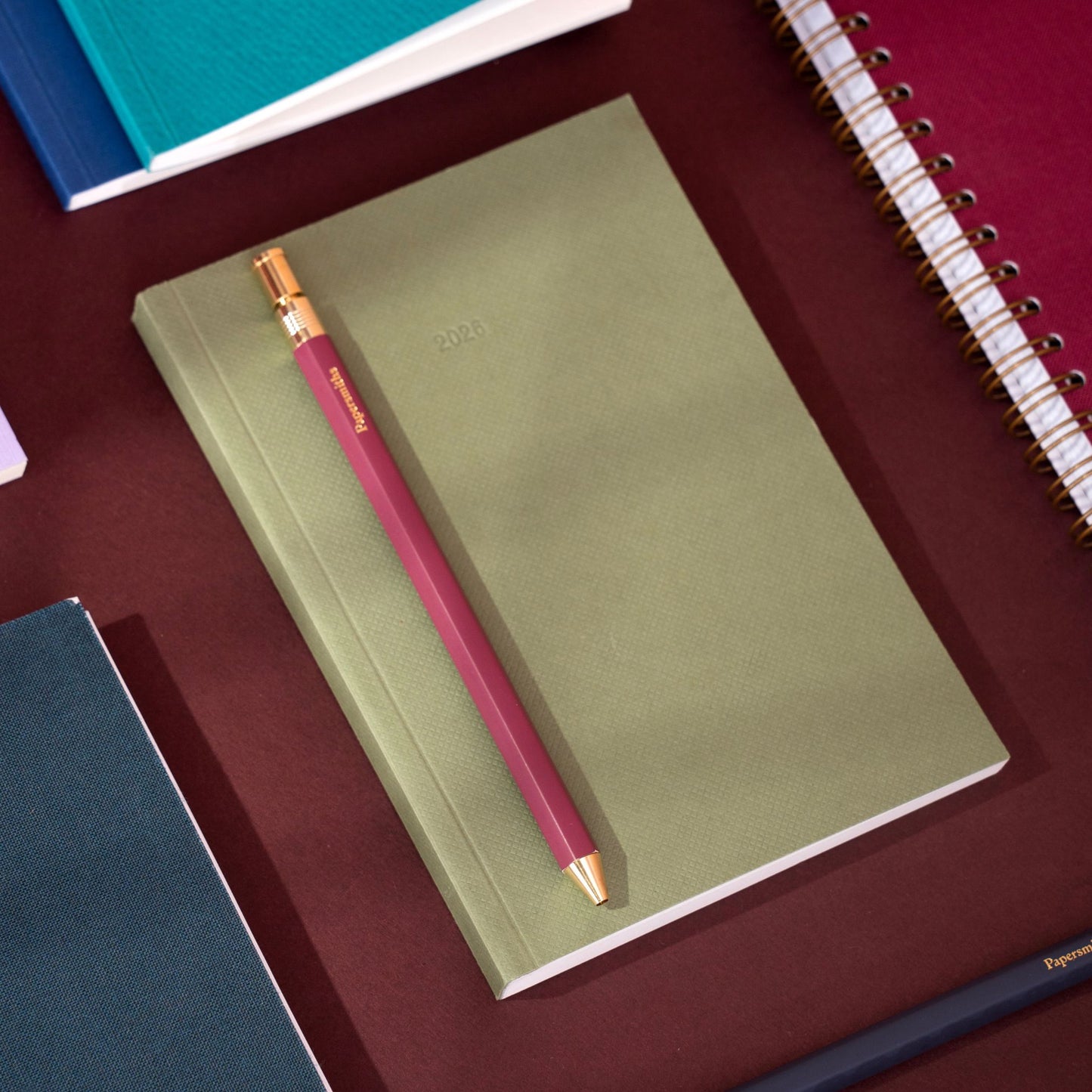 Green notebook with a pink pen on a red surface