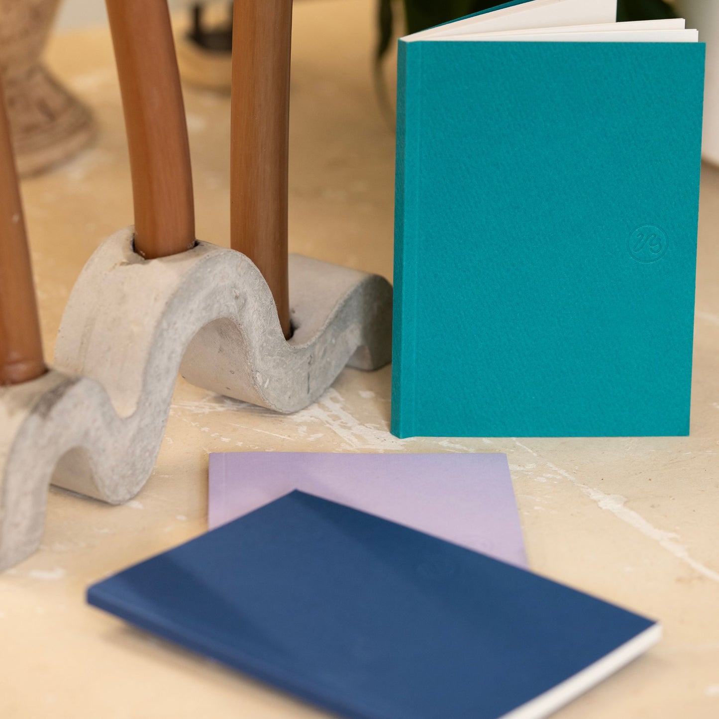 Teal notebook with two other notebooks on a textured surface