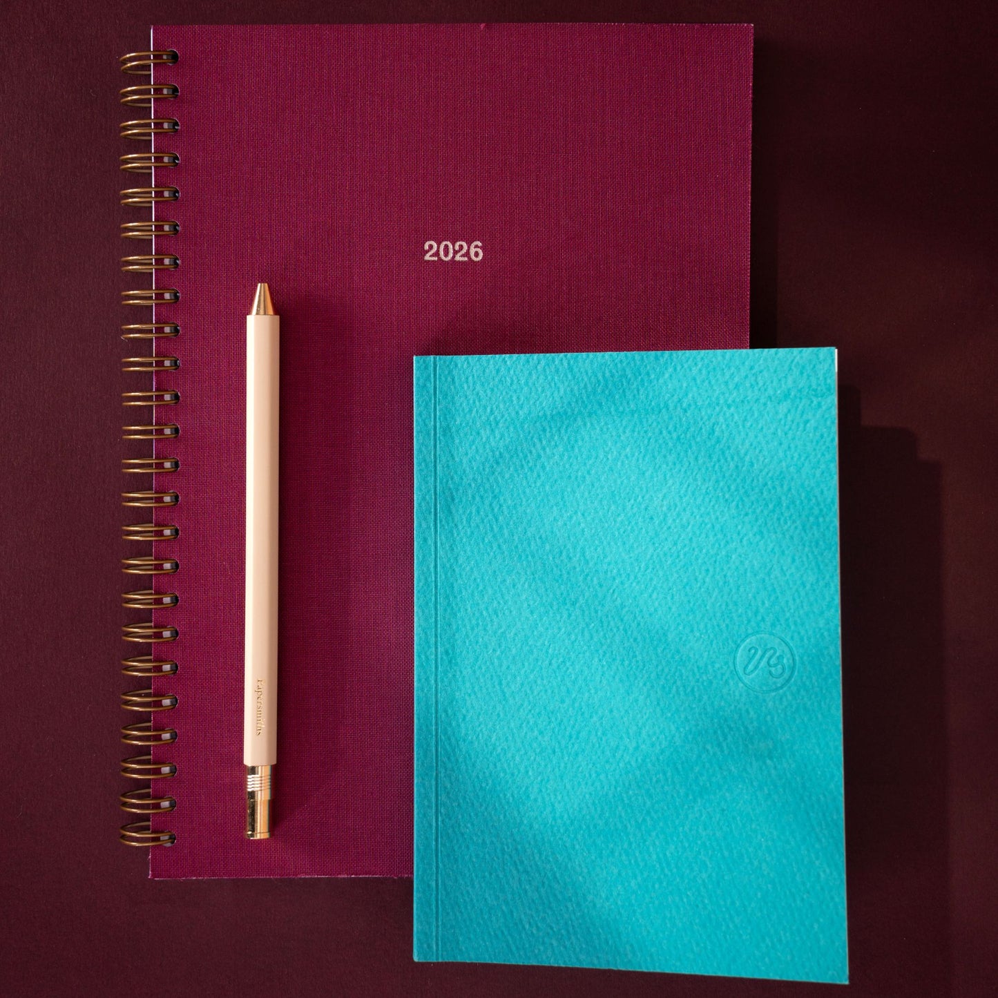 Two notebooks, one burgundy red and one blue, with a pen on a dark background